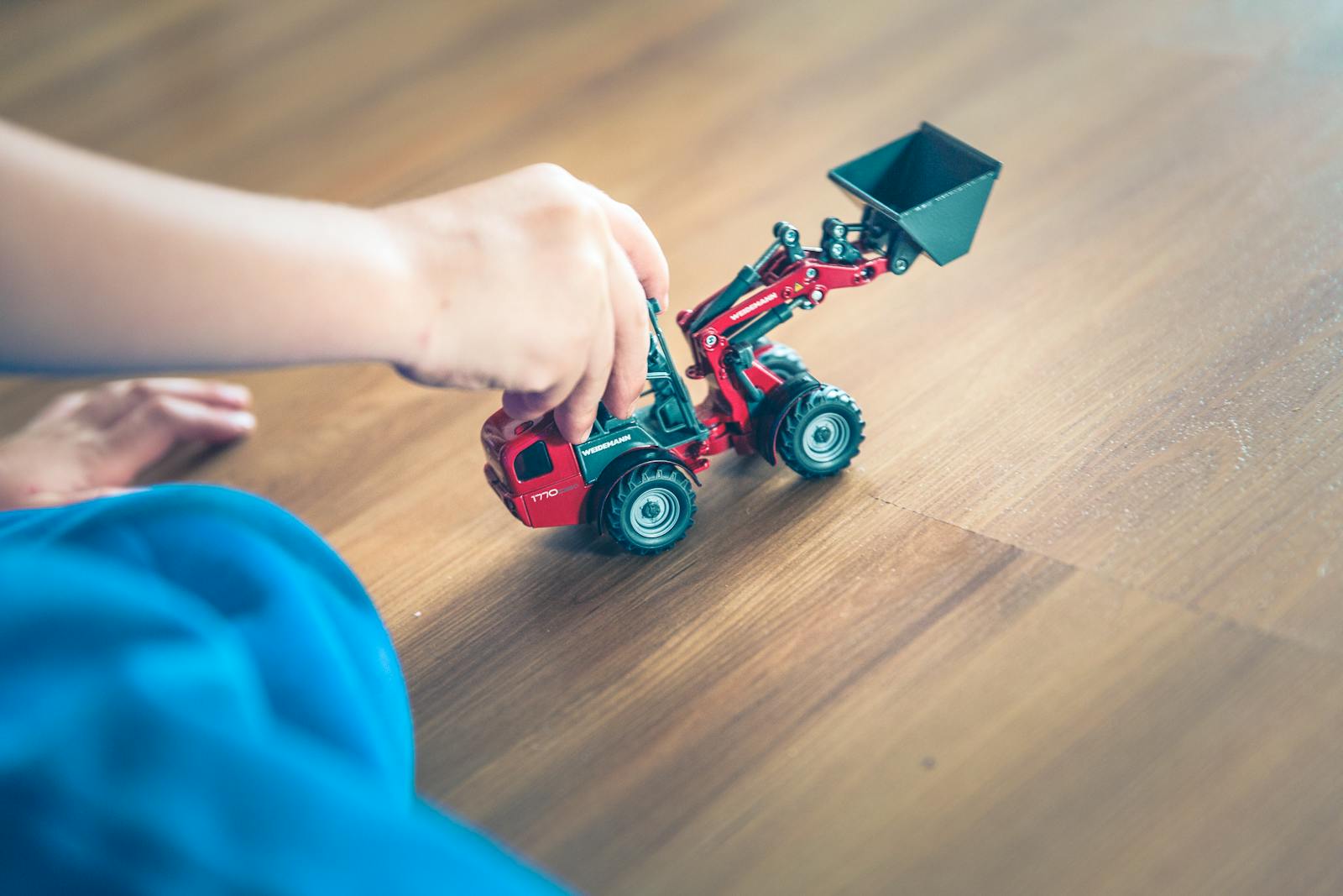 A child plays with a toy excavator on a wooden floor, enjoying creative indoor playtime.
